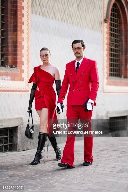 Guest wears sunglasses, a piercing, long black gloves, a red one-shoulder mini dress, a black bag, black pointy under-the-knee high-heeled Balenciaga...