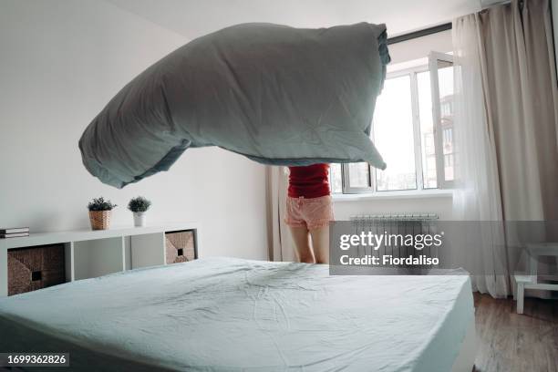 a woman makes her bed, the sheet billowing in the air above the mattress. household chores, housewife or housekeeper cleaning the apartment - piumone foto e immagini stock
