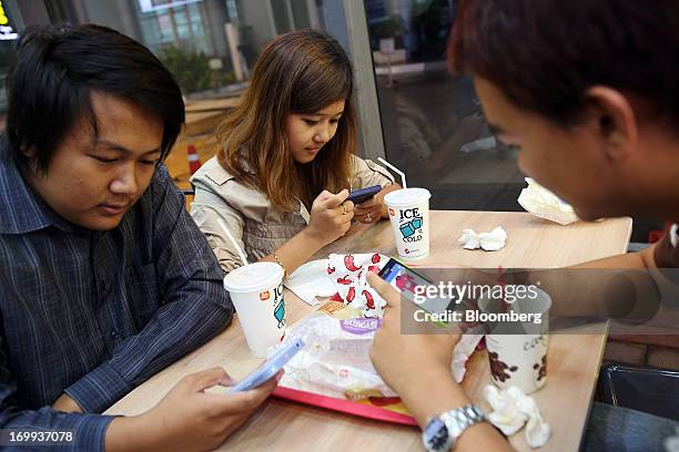Htet Wai Than Htay, left, Aye Myat Thu, center, and Myat Thiha use their mobile phones as they sit inside a Lotteria Co. Restaurant at the Junction...