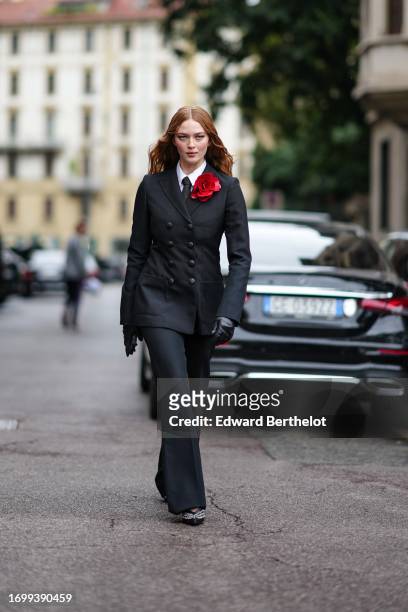 Larsen Thompson wears a white shirt, a black tie, a black oversized double breasted blazer jacket, leather gloves, suit pants, outside Philosophy Di...