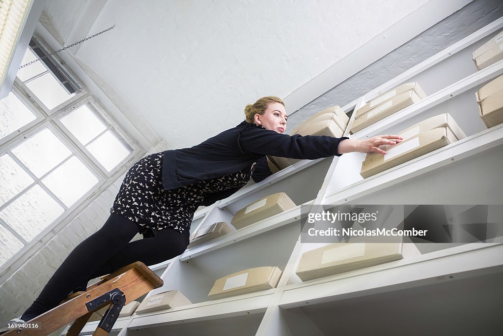 Donna su una scala di raggiungere una scatola di raggiungere