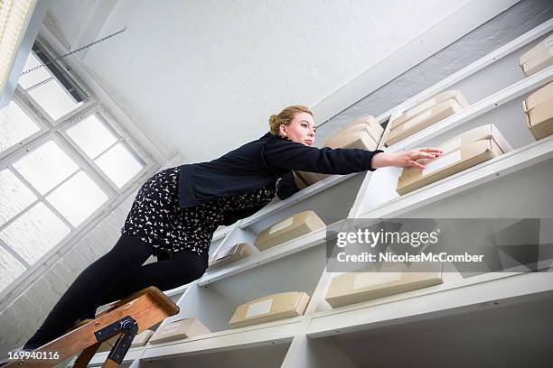 woman on a ladder reaching for a box out of reach - danger 個照片及圖片檔