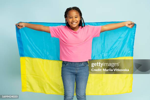 Portrait of smiling beautiful African girl holding Ukrainian flag wearing casual t shirt and jeans