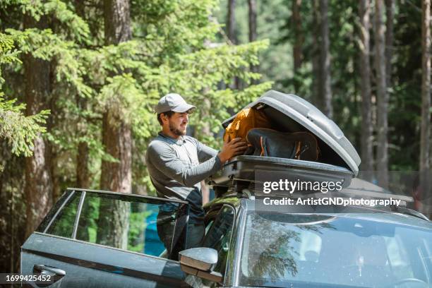 man filling cargo box container on roof rack for camping vacation. - achterbak-van-auto stockfoto's en -beelden