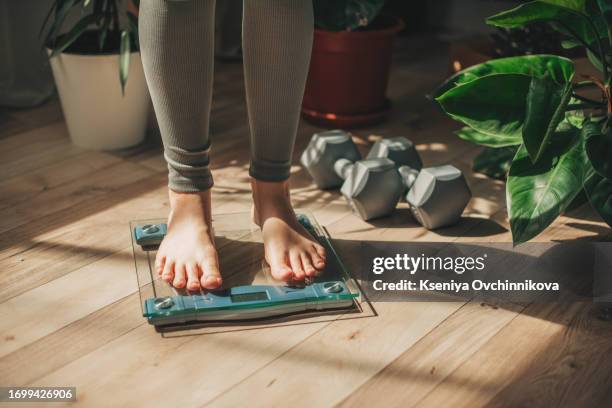 a young woman is weighing herself in a weighing scale - gewicht meeteenheid stockfoto's en -beelden