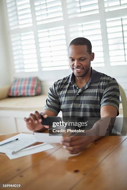 hombre mediante teléfono móvil al depósito de banco múltiple - bank deposit slip fotografías e imágenes de stock