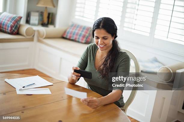 woman using smart phone to deposit check at home - cheque deposit stock pictures, royalty-free photos & images