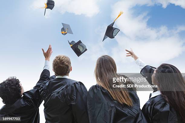 aufgeregt gruppe von college-absolventen werfen ihre hüte in celebration - graduation hat stock-fotos und bilder