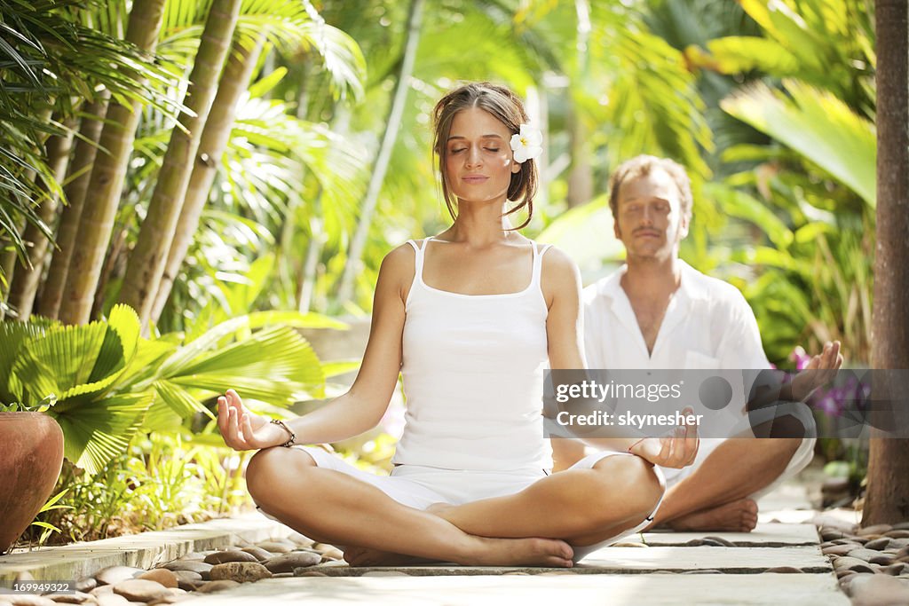 Beautiful couple meditating in the tropical surroundings