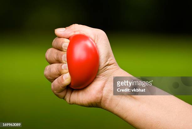 hand squeezing a red stress ball - stress ball stock pictures, royalty-free photos & images