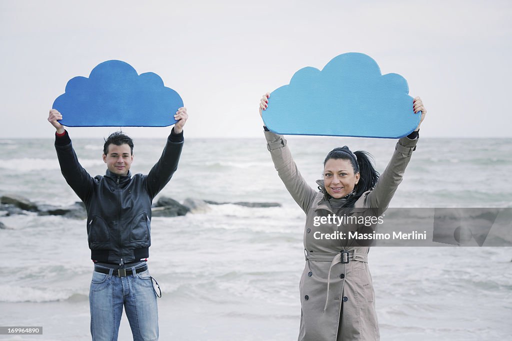 Man and woman on a beach holding up foam clouds
