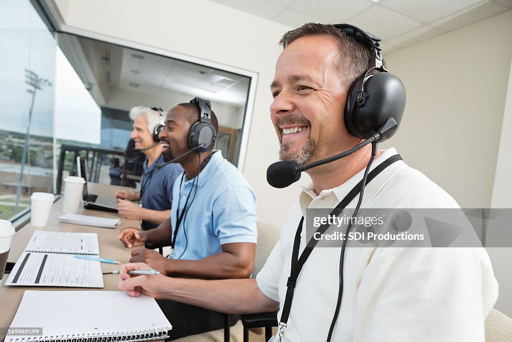 Sports commentators wearing headsets; reporting from stadium press box