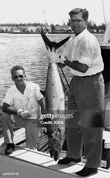 Man stands on the stern of a fishing boat holding a 51 pound king mackerel caught in waters off San Juan, Puerto Rico on September 23, 1951.