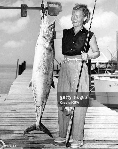 Woman stands on the dock holding her fishing rod and weighing her 44 pound king mackerel caught on 30 pound line in waters near Bimini, Bahamas on...
