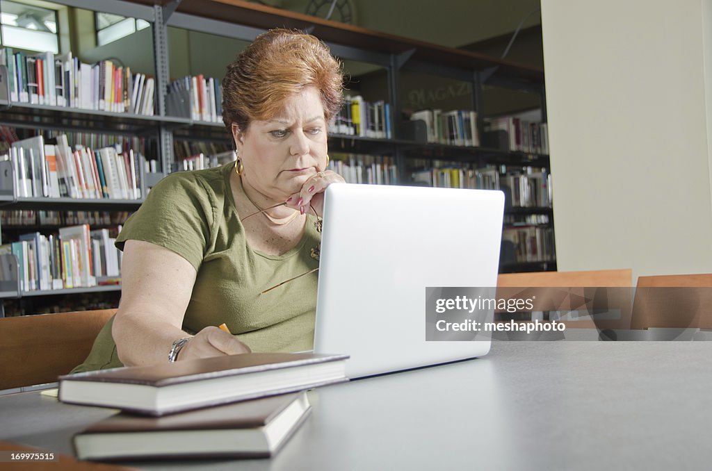 Mulher idosa com computador portátil na biblioteca