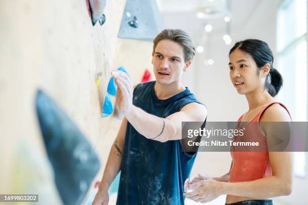 rock climbing gyms help your mind and body. a male climbing instructor discusses and advises a female climber to give basic instructions in front of artificial climbing walls in an indoor climbing gym. - chalk wall stock pictures, royalty-free photos & images