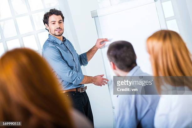 young businessman presenting his ideas on flip chart to colleagues - flipchart stock pictures, royalty-free photos & images