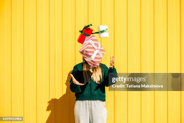 woman in christmas hat and green sweater catching christmas gift box against the yellow wall. funny summer christmas and sales concept. - cadeau photos et images de collection