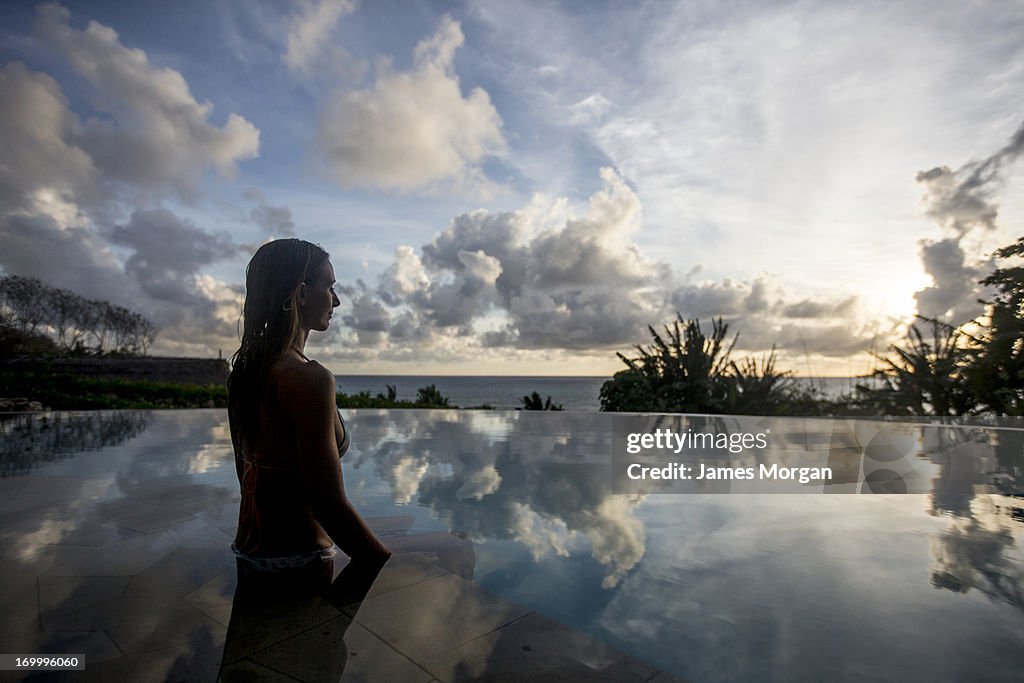 Woman sat in infinity pool with cloud reflections