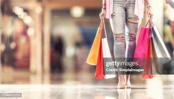 full shopping bags in the hands of a shoppers woman and her legs jeans and shoes in shopping mall. - accro du shopping photos et images de collection
