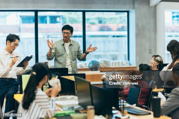 ein asiatischer mann führt eine diskussion mit seinen kollegen in einem kreativbüro, in der sie gemeinsam brainstormen, herausforderungen meistern und lösungen finden. - brainstormen stock-fotos und bilder