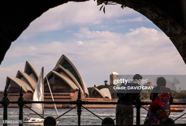 Couple watches boats as they stand on the harbour foreshore opposite the Sydney Opera House in Sydney on October 1, 2023 as the country sweltered in...