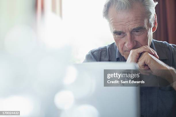 uomo anziano con le mani intrecciate utilizzando un computer portatile - preoccupato foto e immagini stock