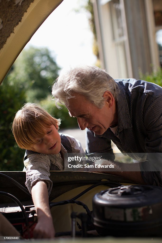 Grandfather and grandson looking under automobile hood