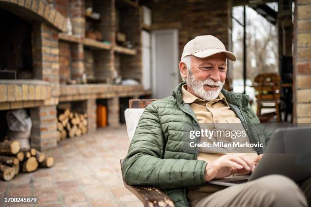 a pensioner sits on the terrace of a cottage and works on a laptop - old man smart stock pictures, royalty-free photos & images