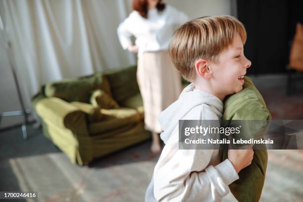 dynamic family scene: boy runs around with pillow while his parents get up sofa - teasing stock pictures, royalty-free photos & images