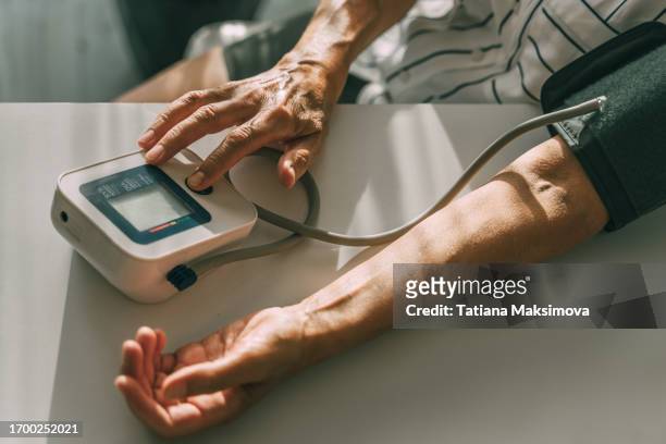 an elderly woman takes her blood pressure at home. - blood pressure photos et images de collection