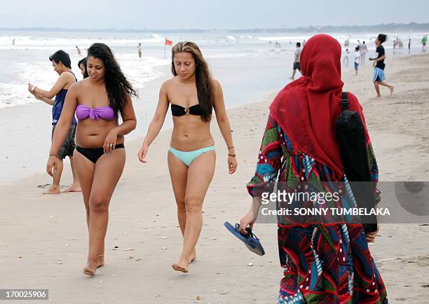 Muslim woman wearing a veil walks past foreign tourists wearing bikinis on Kuta beach near Denpasar on Indonesia's resort island of Bali on June 6,...