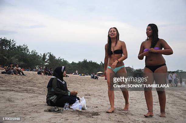 Foreign tourists wearing bikinis walk past a Muslim woman sitting on Kuta beach near Denpasar on Indonesia's resort island of Bali on June 6, 2013....