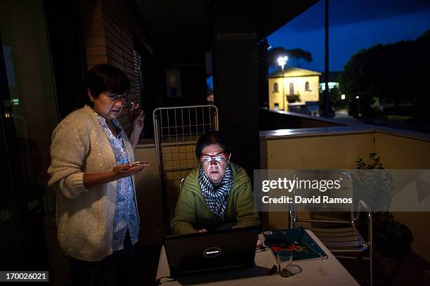 Fifty-one year old Doris Perez and fifty-three year old Engracia Casellas look at her laptop on the balcony of the apartment of an occupied newly...