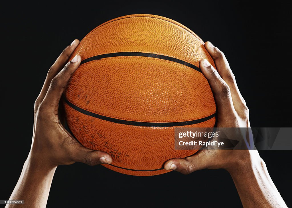 Male hands hold up a basketball against black