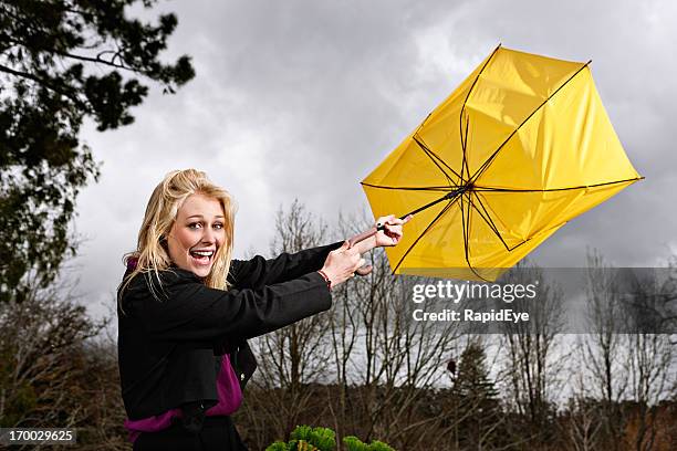 beautiful blonde laughs as wind blows umbrella inside out - broken umbrella stockfoto's en -beelden