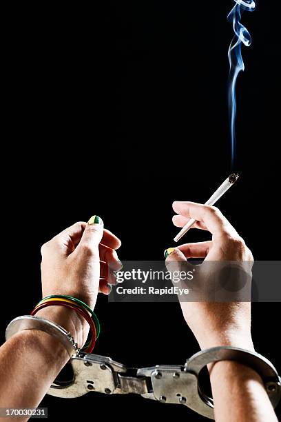 the drug trap: handcuffed female hands holding lit marijuana cigarette - marijuana arrest stock pictures, royalty-free photos & images