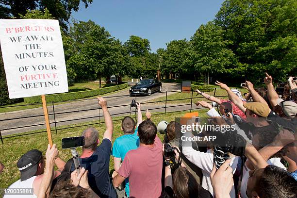 Protesters shout and wave a placard that reads "B'Bergers, we await the minutes of your furtive meeting” as a vehicle arrives at the drive to the...