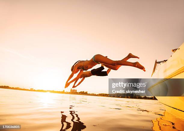 deux personnes sautant dans l'eau avec la lumière du soleil. - jumping of boat photos et images de collection