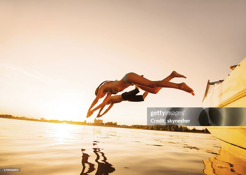 Two people jumping in water against the sunlight.