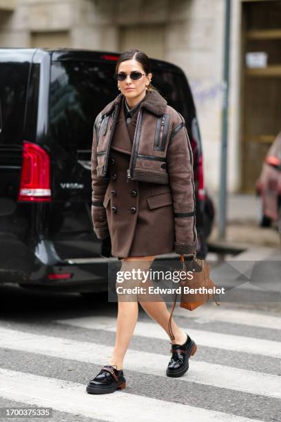 Paola Alberdi wears sunglasses, a brown aviator winter jacket, a brown double breasted coat, black leather shoes, a brown bag, outside Tod's, during...