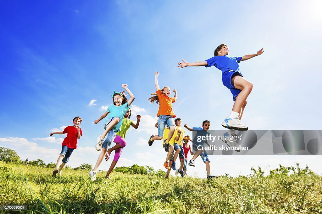 Cheerful kids jumping in field against the sky.