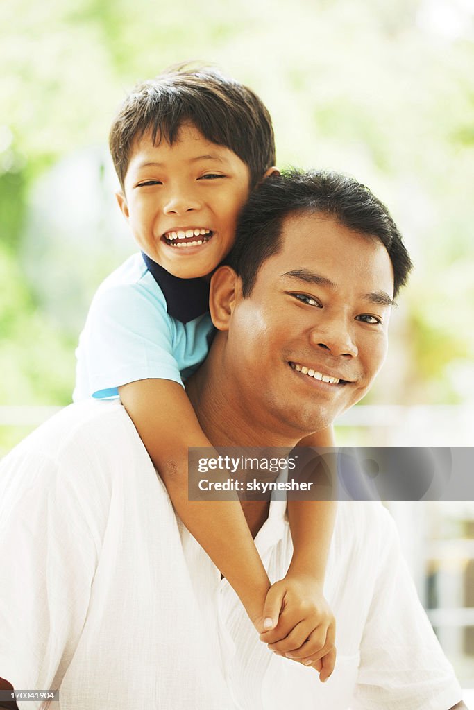 Thai father carrying giving his son a piggyback ride.