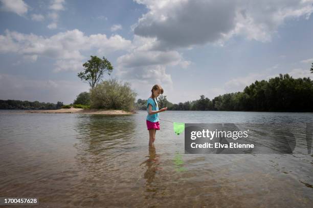 girl (10-11 years) standing in the shallow waters near the shore of a lake on a beautiful summer's day, holding a toy fishing net whilst examining a found shell in her hands. - 10 11 years stock pictures, royalty-free photos & images