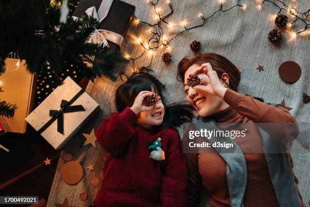 top view of asian mother and lovely daughter enjoying together while lying on the floor under decorated christmas tree at christmas time. christmas lifestyle theme. family celebrating christmas. holiday and festive vibes - 2 5 months 個照片及圖片檔