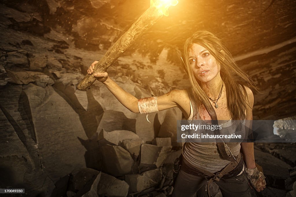 Female heroine looking in a cave with torch