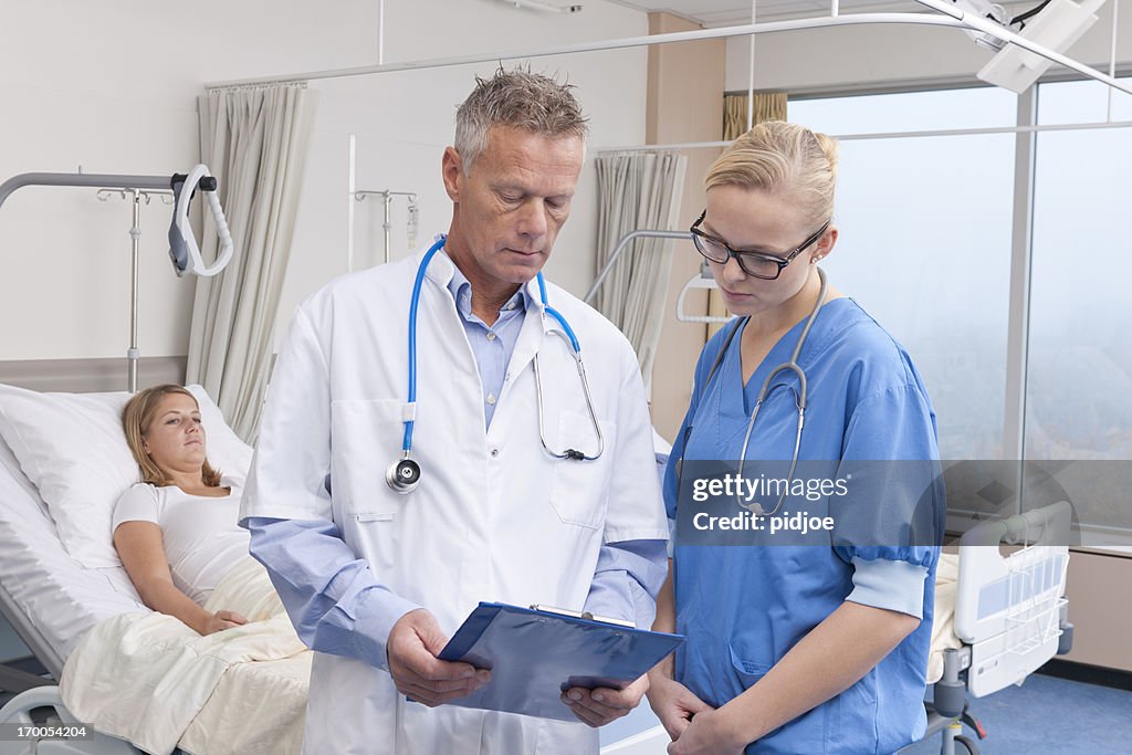 Doctors checking medical chart of patient on hospital ward