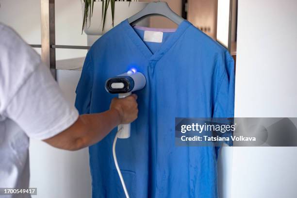 unrecognizable mature woman carefully employs steamer to perfect medical scrubs - medical scrubs hanger stock pictures, royalty-free photos & images