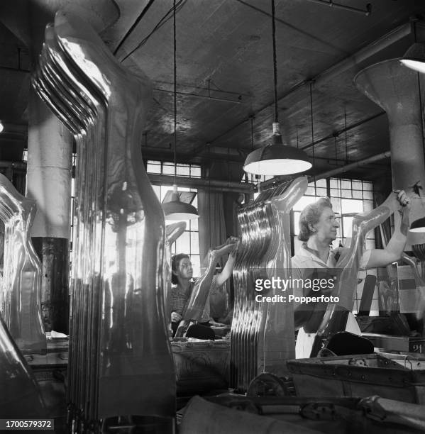 Female workers place still wet dyed nylon stockings onto electrically heated aluminium shapes to dry and press the items at a hosiery factory in the...