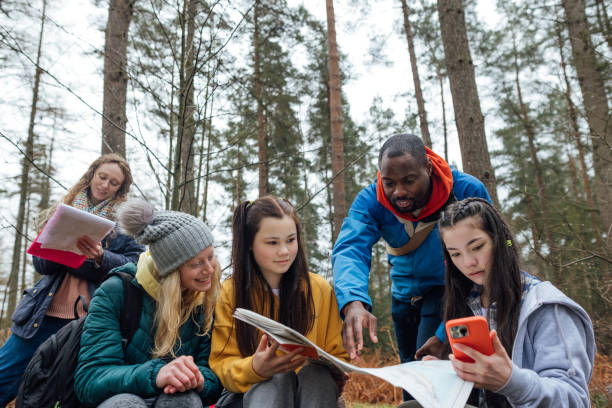 Group of middle grade age youths and a teacher reading a map in the forest